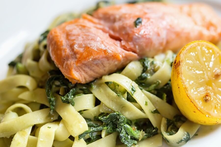 Beautifully cooked, flaky salmon sitting luxuriously atop a bed of herbed fettuccine, with a baked half lemon