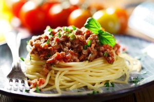 Delicious lean turkey pasta sauce, draped elegantly over fresh pasta on a plate with a silver metal fork, on a backdrop of tomatoes.
