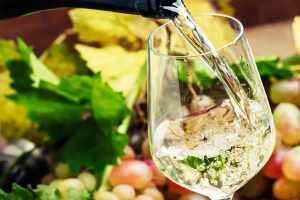 Riesling Wine - A beautifully clear Riesling wine being poured wonderfully into a wine glass on a backdrop of fruit!