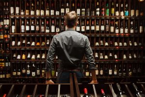 A man staring at a wall of amazing wines, looking for Cheap Wine Deals!