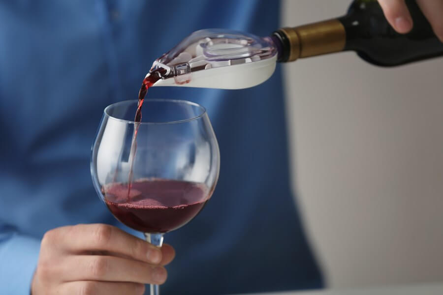 A man pouring wine into a beautiful wineglass through a wine aerator.